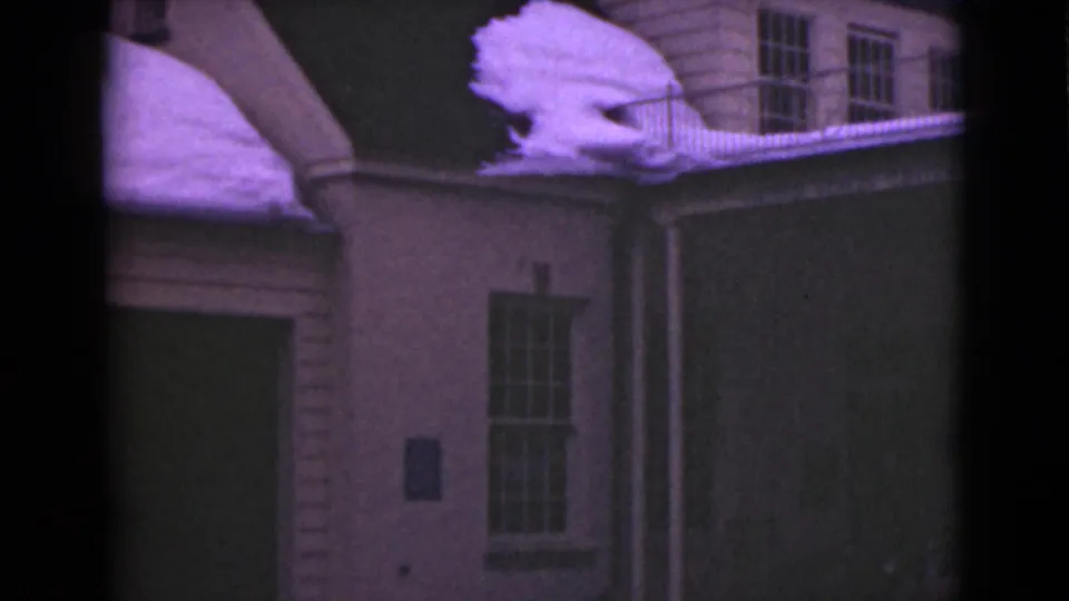 1946 Alaska 8mm frame showing a closer portion of the snow-covered roofline, clapboard siding, tall divided window, and dark exterior wall area.