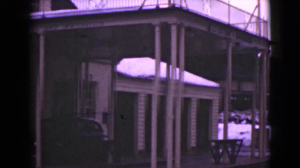 1946 Alaska 8mm frame of a wooden building's porch, columns, upper railing, snow patches, side structure, and parked car.