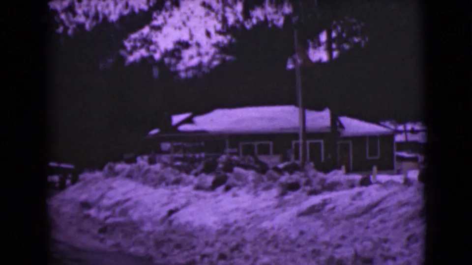 1946 Alaska 8mm frame of a snow-covered house and deep roadside snow, with trees behind and a dark object at left.
