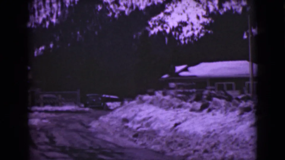 1946 Alaska 8mm frame with a snowbank in the foreground, a snowy road, a parked car, and a house partly visible to the right.