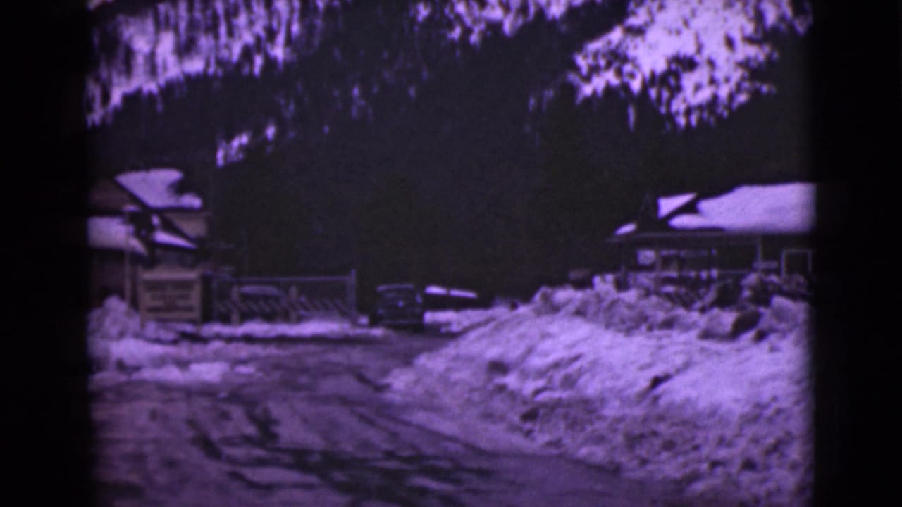 1946 Alaska 8mm frame showing a snow-covered building near a plowed road, with trees and heavy snowbanks around it.