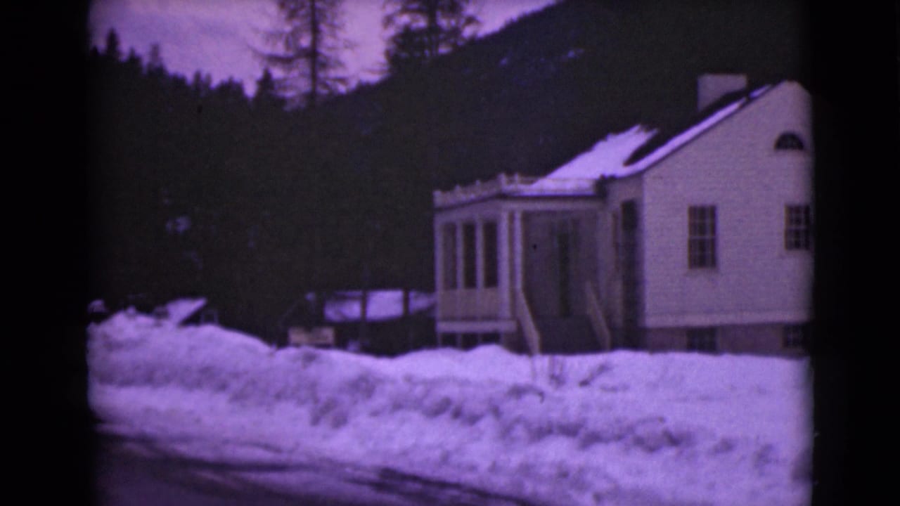 1946 Alaska frame showing a house exterior, porch, roadside snowbanks, trees, and a dark hillside under winter light.