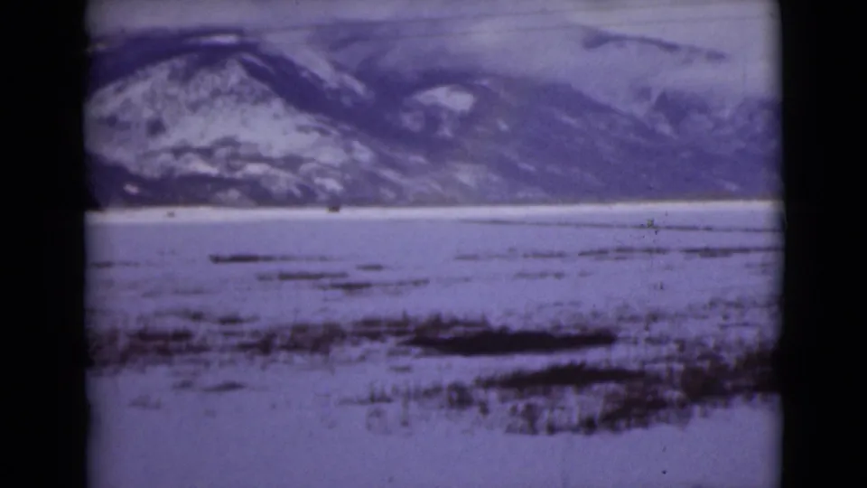 1946 Alaska home-movie frame of snow-covered flats and distant mountains under a clouded winter sky.