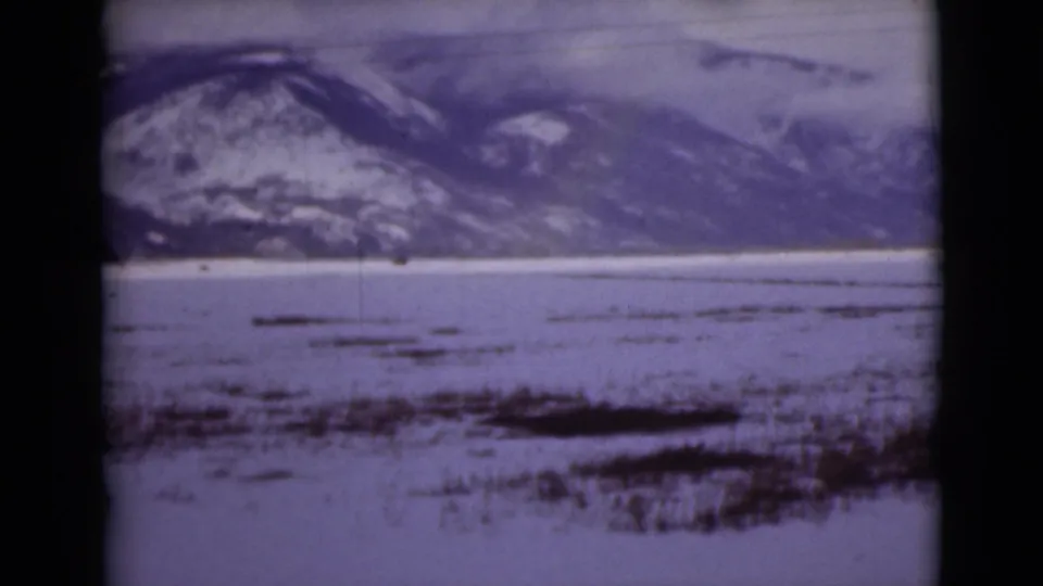 1946 Alaska home-movie frame showing a broad snowy flat foreground and mountain slope in the distance.