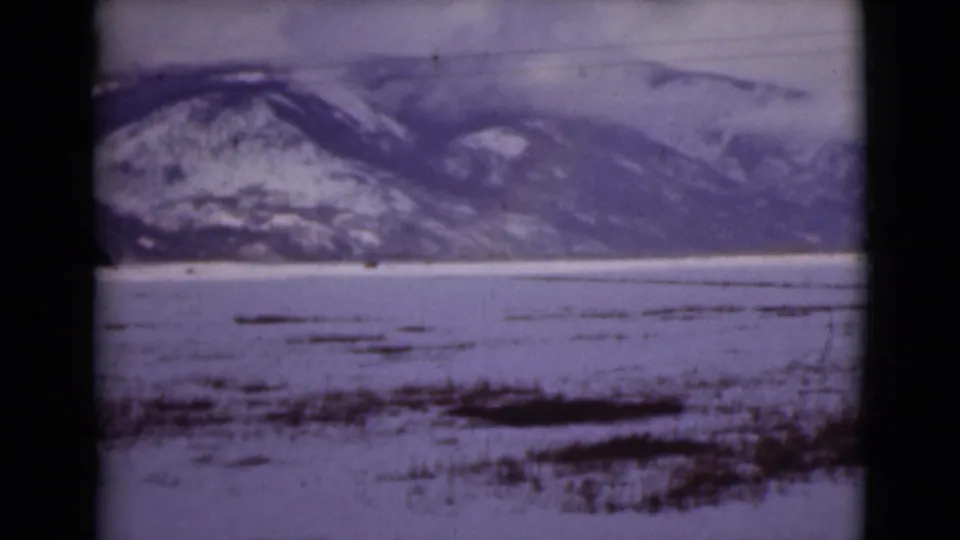 1946 Alaska home-movie frame of open snowy flats, scattered dark vegetation, and distant mountains.