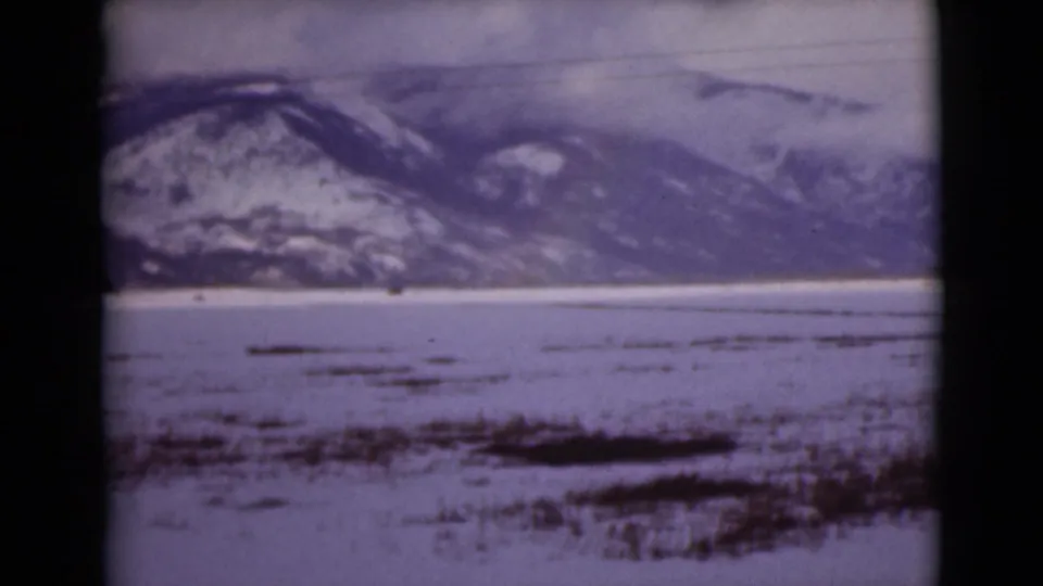 1946 Alaska 8mm frame showing snow-covered mountains across a frozen tundra or lake, with dark exposed patches in the foreground.