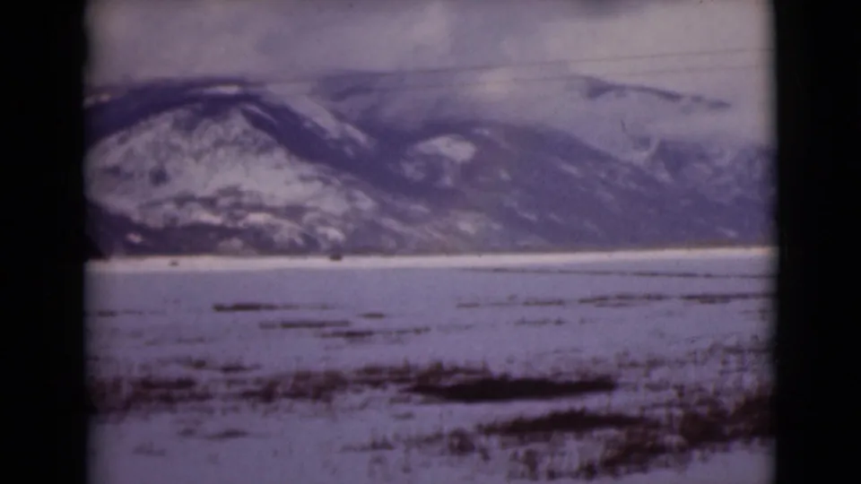 1946 Alaska 8mm still showing distant snowy mountains, a frozen tundra or lake surface, and scattered dark vegetation in the foreground.