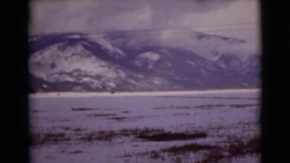 Final 1946 Alaska frame with snow-covered mountains, cloudy sky, and a frozen tundra or lake foreground marked by dark vegetation.