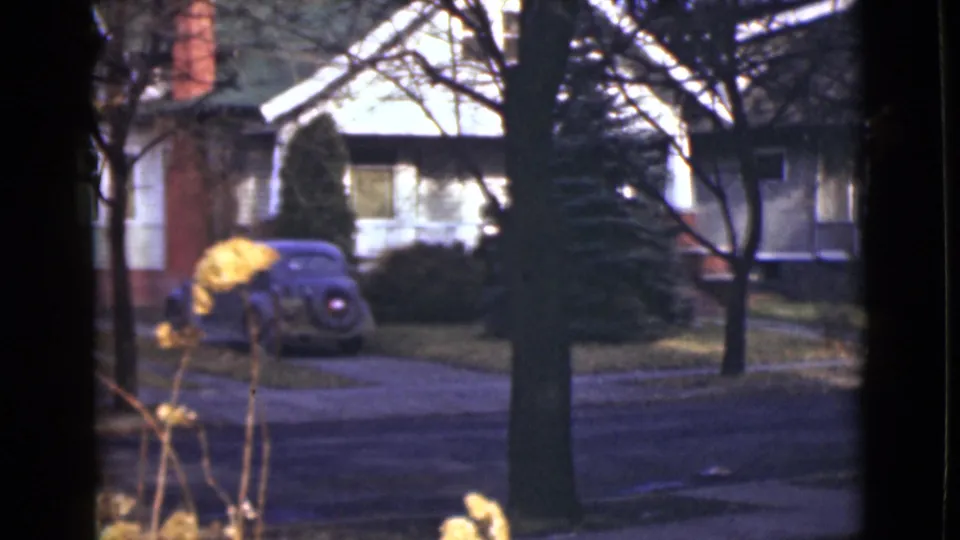 1946 Alaska 8mm frame showing a rounded parked car in a driveway across a quiet residential street with trees and houses.