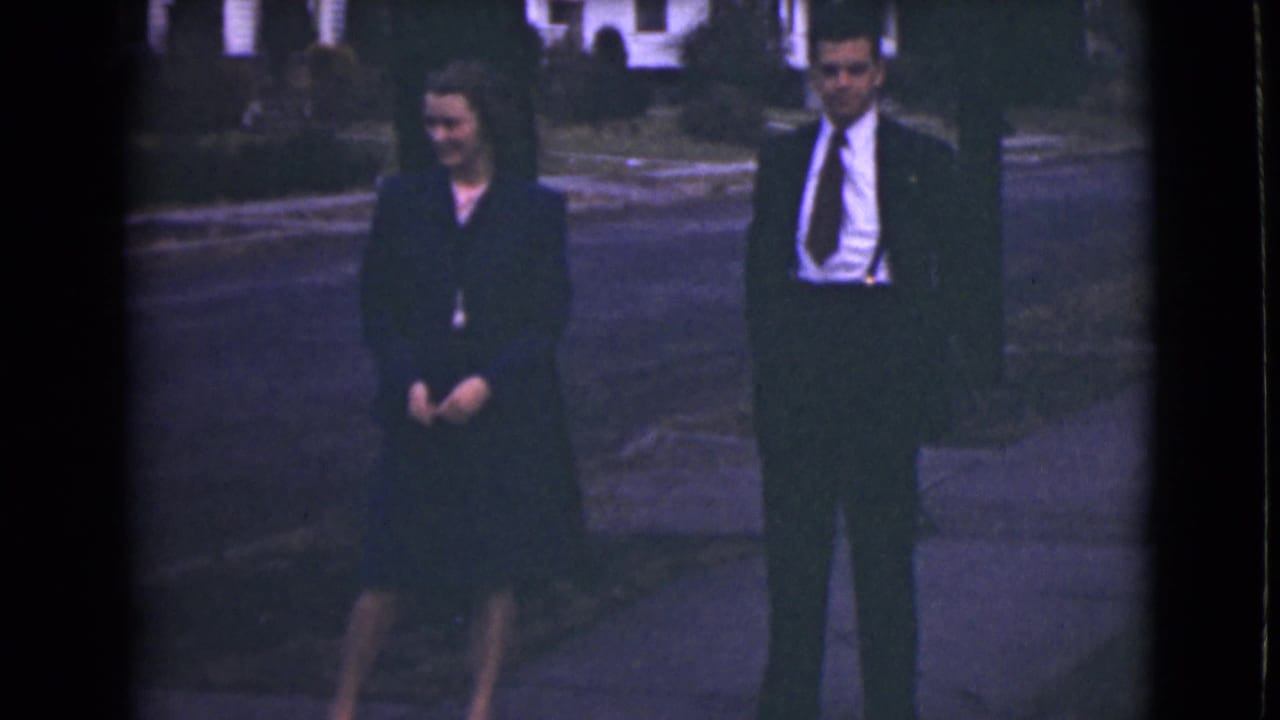 A woman and man in formal dark clothing stand on a sidewalk.