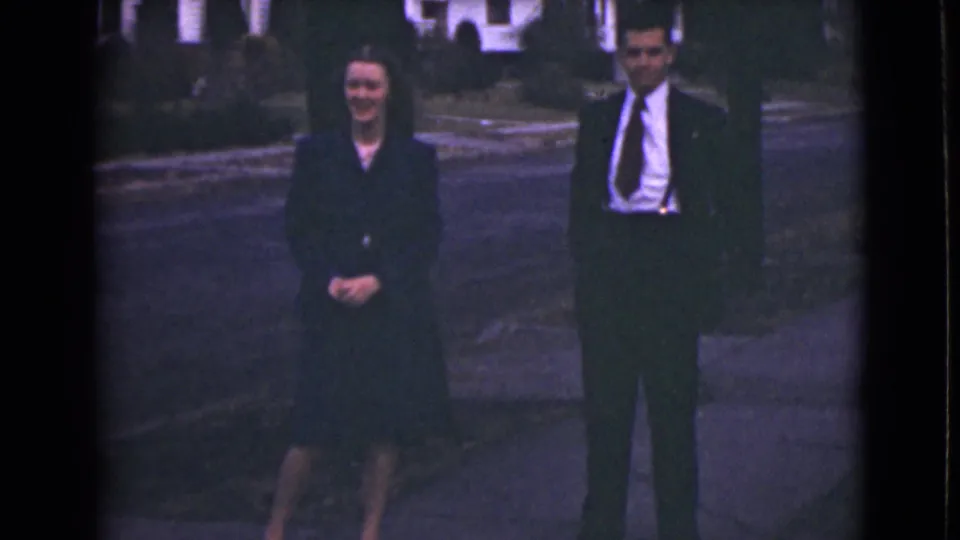 The couple remain on the Alaska sidewalk, with the woman smiling and the man standing formally beside her.
