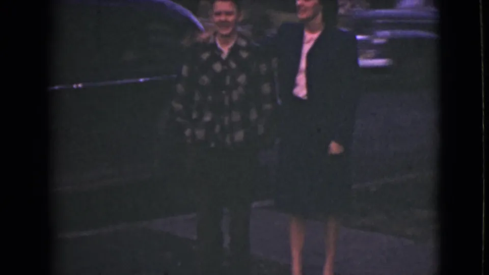 A man in a patterned shirt joins the suited man and woman near a parked car in the 1946 Alaska home-movie scene.