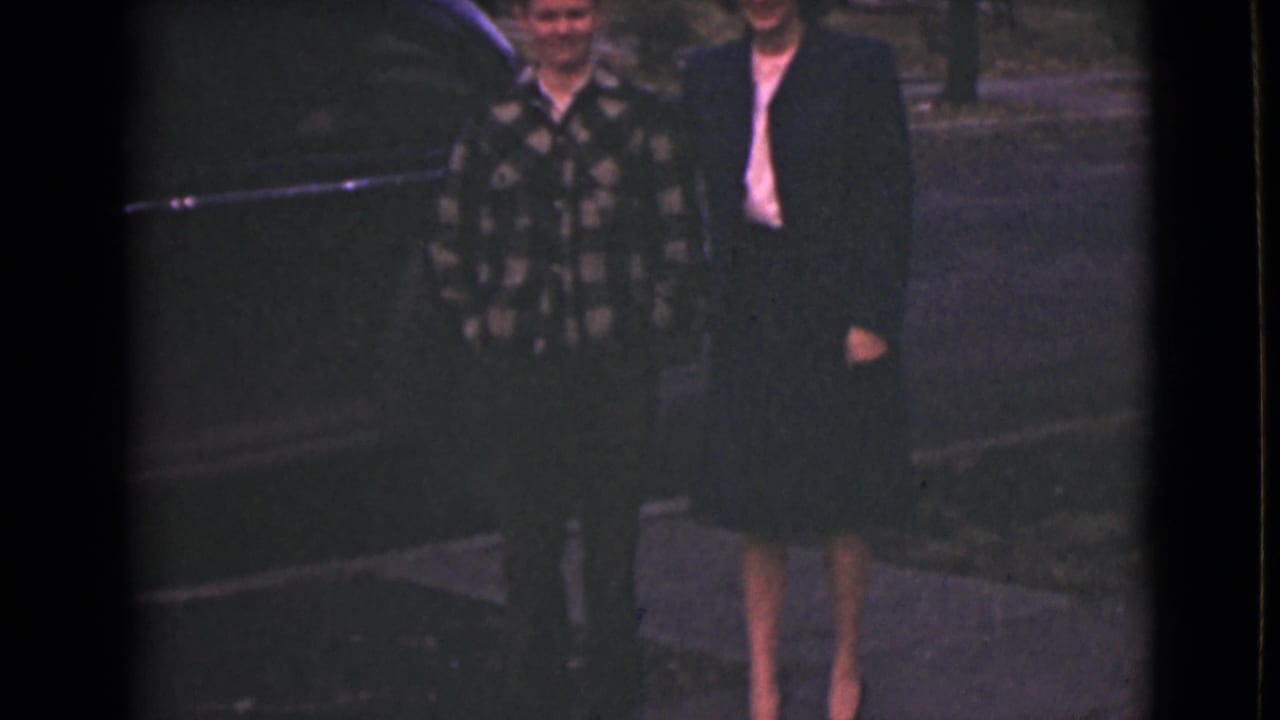In supported 1946 Alaska home-movie footage, an older woman and younger boy stand near a sidewalk on a quiet residential street.