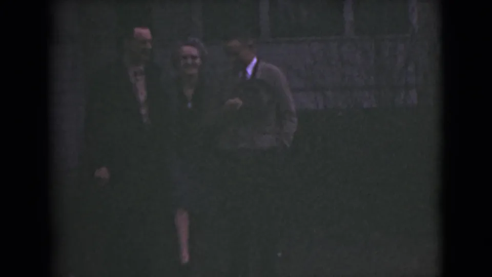 In a dim final frame, several adults gather close together near the same exterior wall, with faces and clothing partly obscured by exposure.