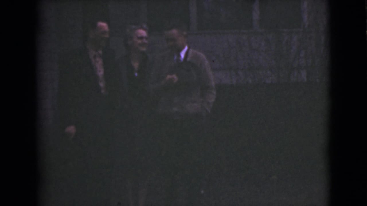 Three adults stand close together in a dim outdoor setting.