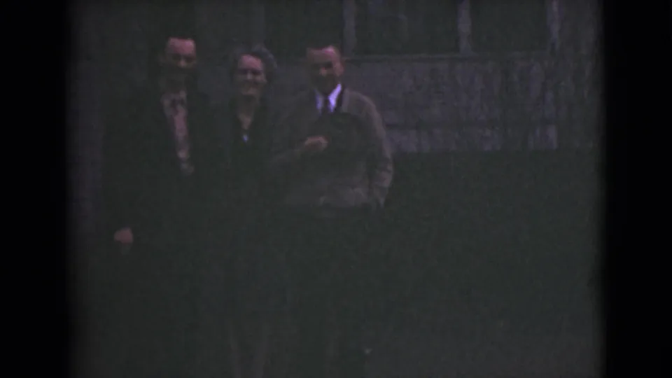 The group remains close together, with a woman in glasses between two suited men in the 1946 Alaska home-movie frame.