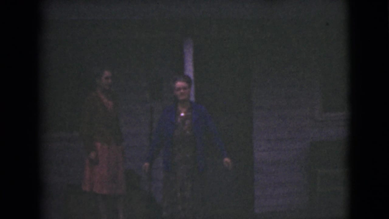 In metadata-supported 1946 Alaska footage, two adult women stand near an exterior doorway or post at night.