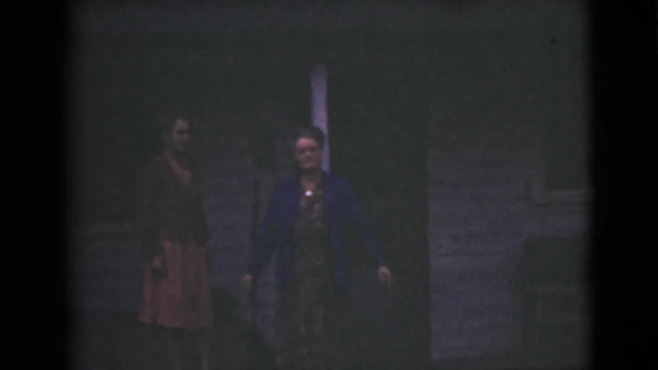 In metadata-supported 1946 Alaska footage, two adult women stand near an exterior doorway or post at night.