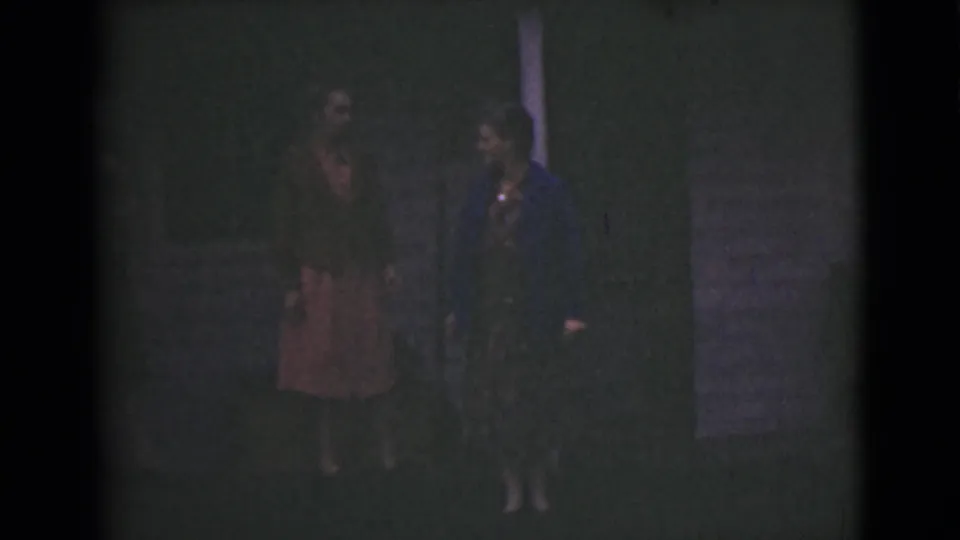 Two adult women in dresses appear near a doorway or exterior post in 1946 Alaska home-movie footage.