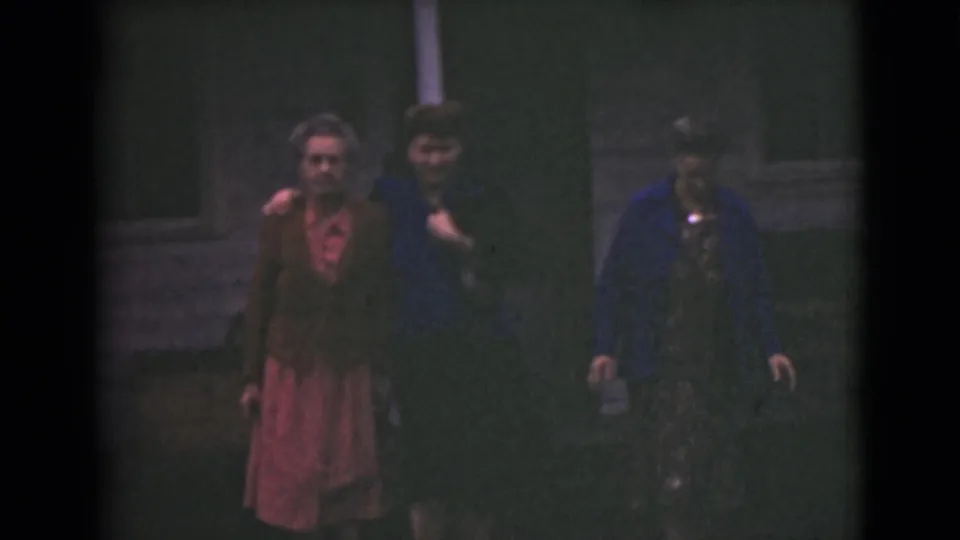Near the end of the 1946 Alaska clip, three women continue walking outside a house, softly lit against dark siding.