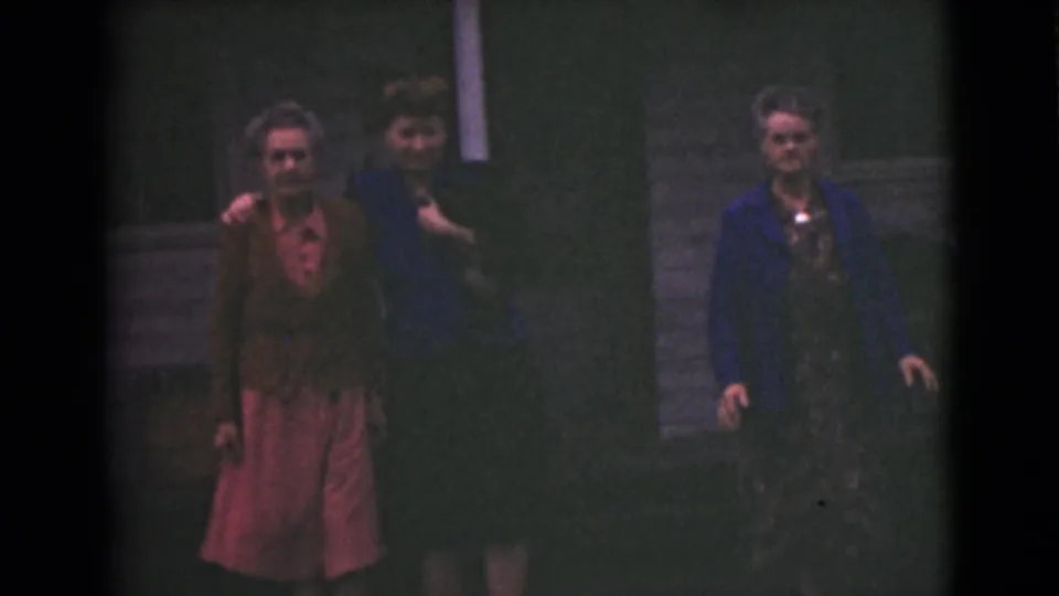 Three older women walk together outdoors in Alaska, with one wearing a brown cardigan over a pink dress.