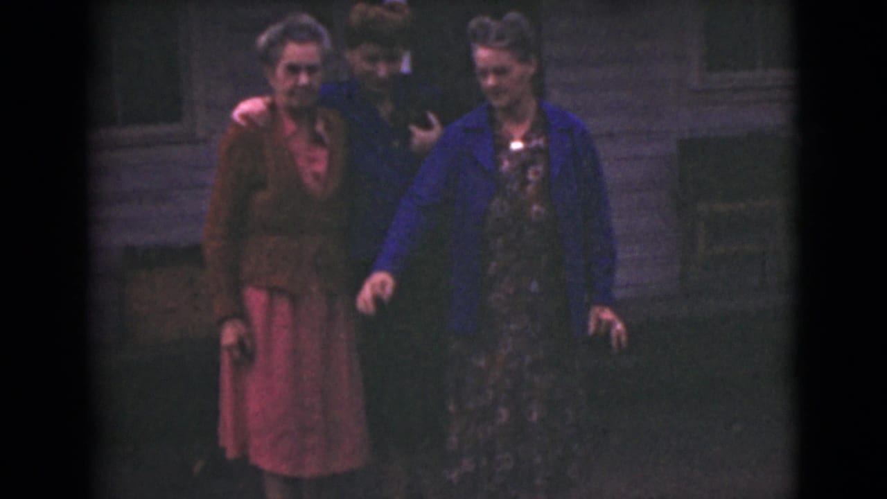 In 1946 Alaska home-movie footage, three adult women gather outdoors, one in a blue jacket and another in a brown cardigan with a pink skirt.