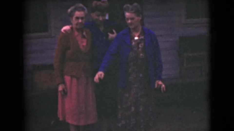 In 1946 Alaska home-movie footage, three adult women gather outdoors, one in a blue jacket and another in a brown cardigan with a pink skirt.
