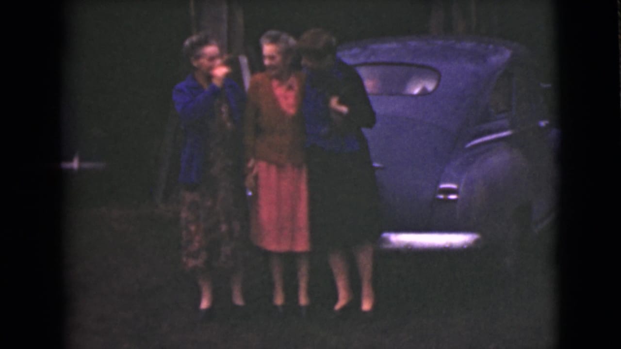 Three adult women in 1940s clothing stand beside a dark car at night or dusk in Alaska, according to clip metadata.