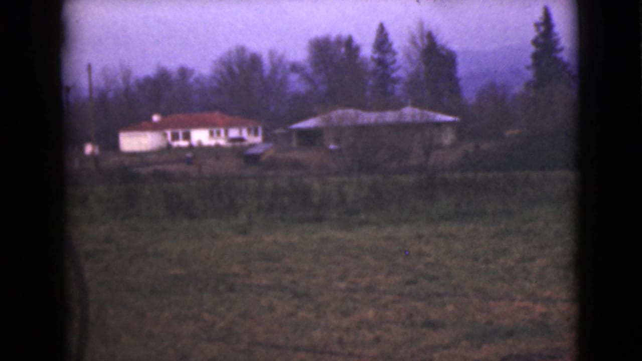 Distant white house with a red roof across a grassy field near trees.