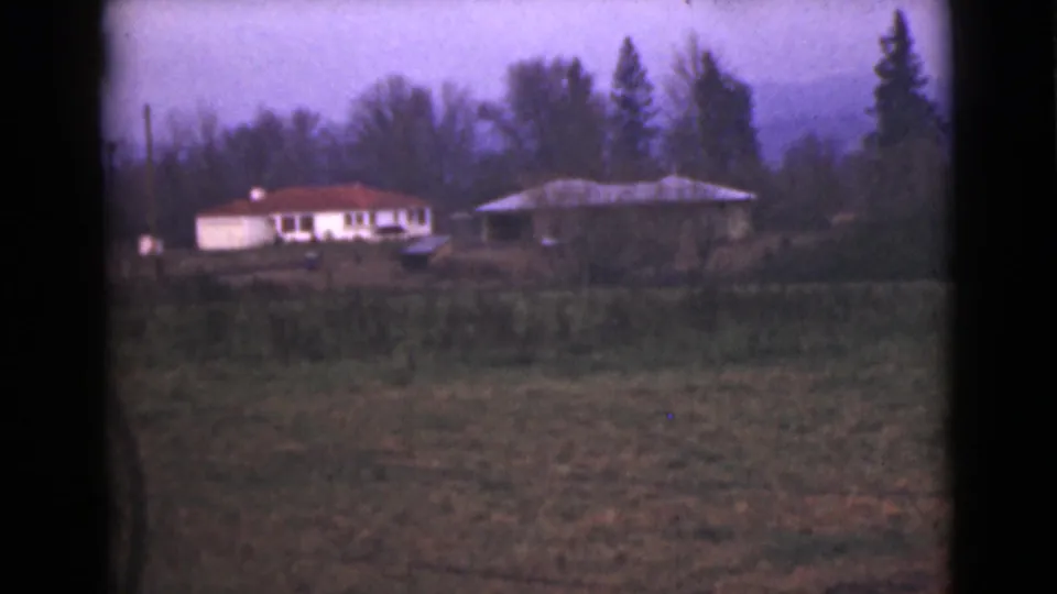 1946 Alaska 8mm frame showing a distant white house with a red roof beside another low structure beyond an open field.
