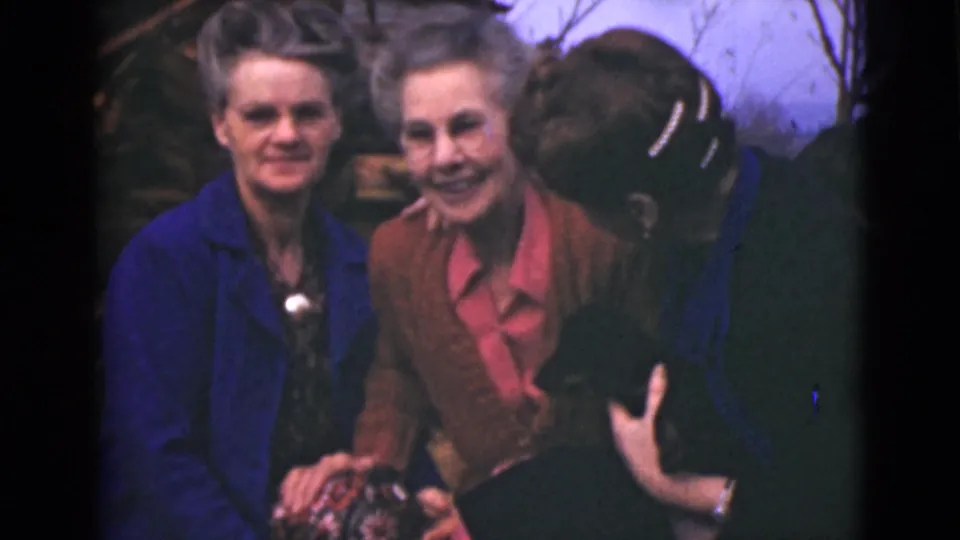 Two older women look toward the camera in 1946 Alaska footage while a third woman leans in closely from the right side.