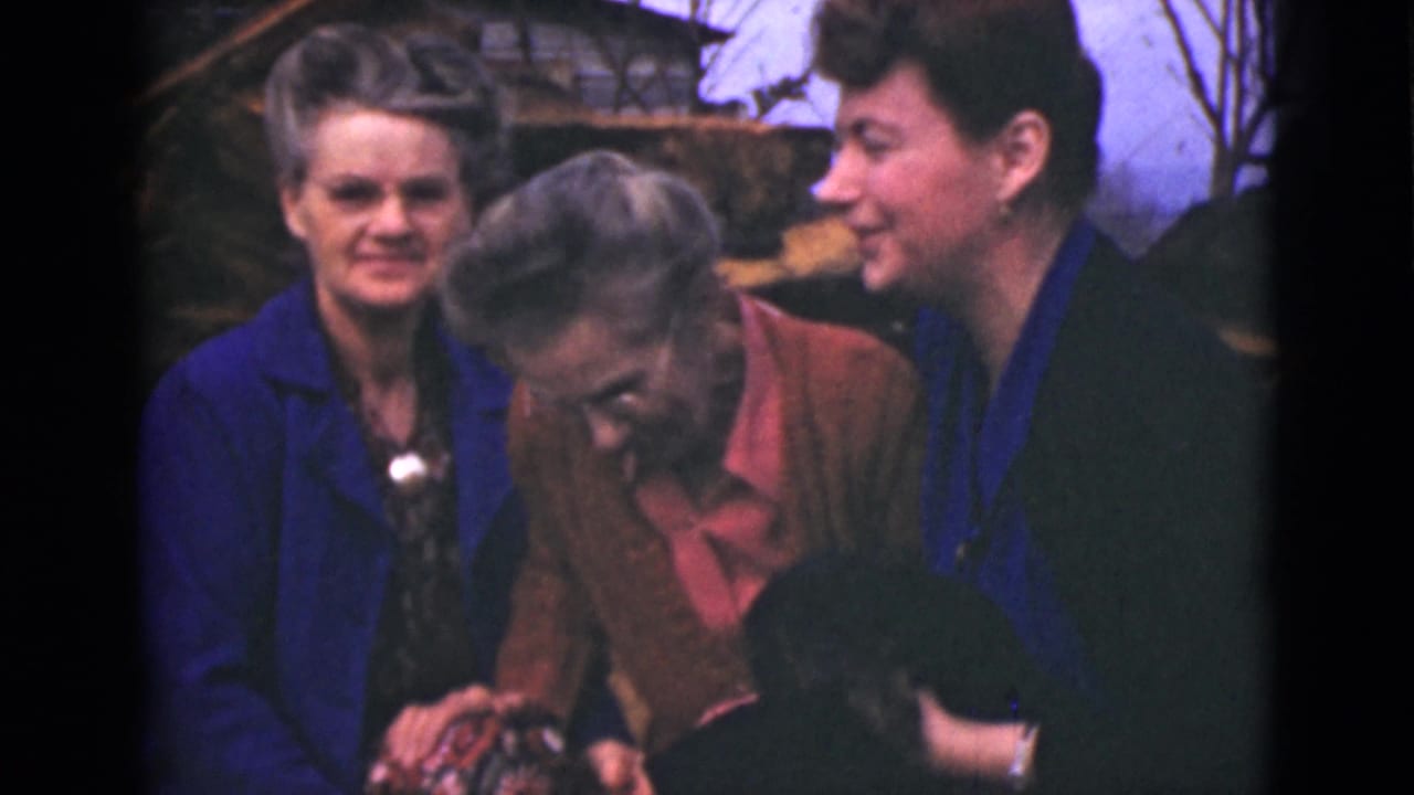 Three women outdoors, with one bending down as another holds a small black animal.