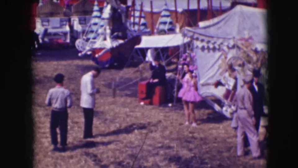 1948 Sarasota circus grounds with a woman in purple posing near canvas tents while photographers and visitors stand nearby.