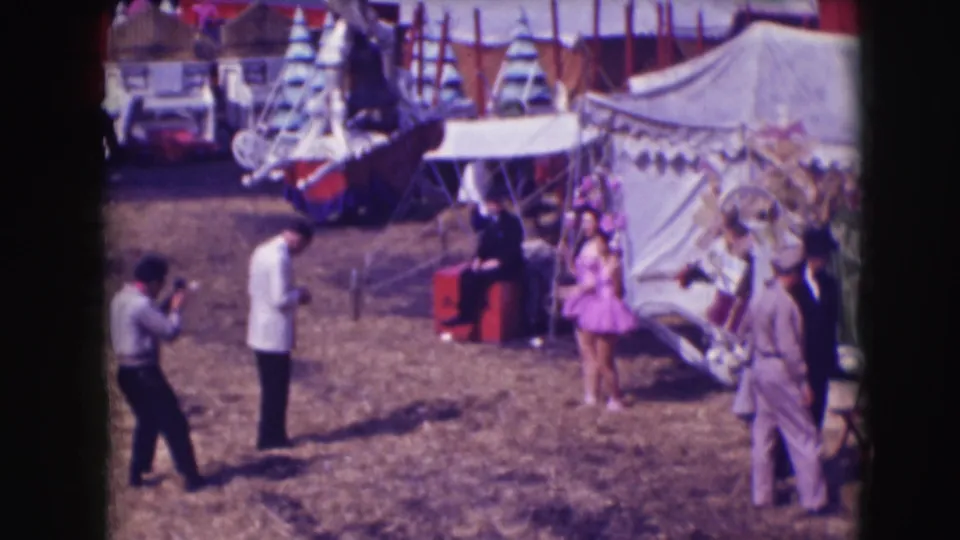 At the 1948 Ringling Brothers Sarasota circus grounds, a photographer aims toward a woman in purple near a tent entrance.