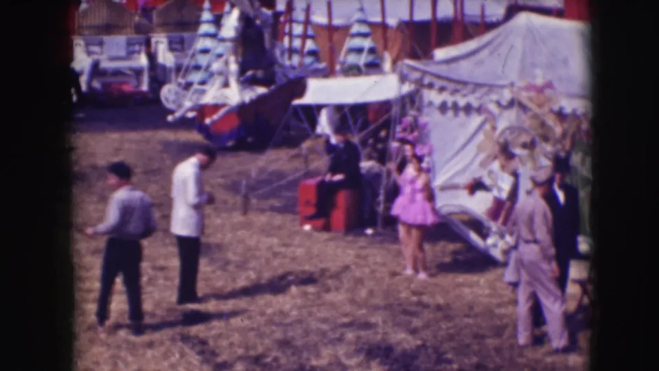 1948 home-movie view of Sarasota circus grounds with photographers, visitors, tents, and the woman in purple near the right edge.