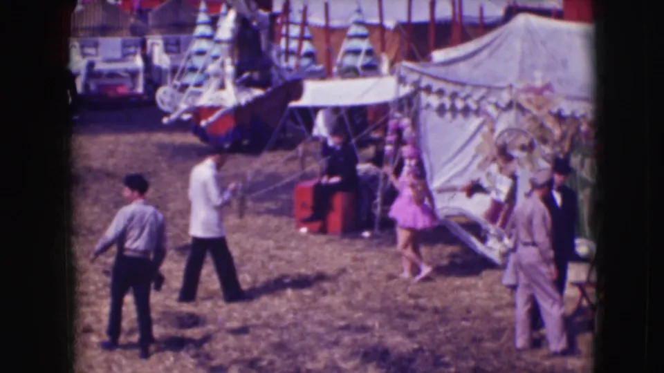 1948 Sarasota circus scene with a foreground visitor walking past photographers and a woman in purple beside tented fairground structures.