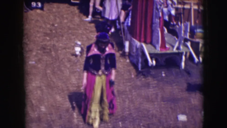 Costumed performer moves through the Ringling Brothers Sarasota backstage area with wagons and people behind them.