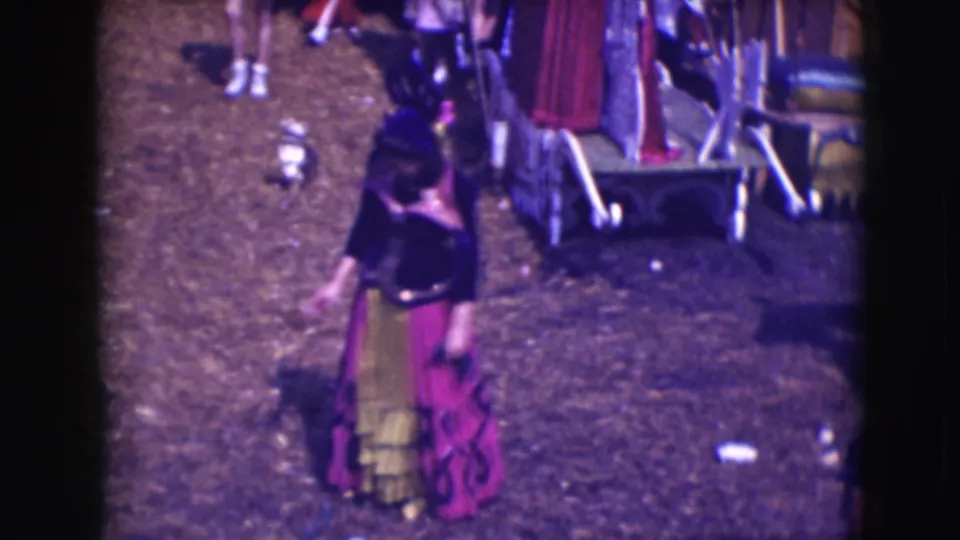A purple and yellow costumed circus performer turns near wagons in 1948 Sarasota Ringling Brothers home-movie footage.