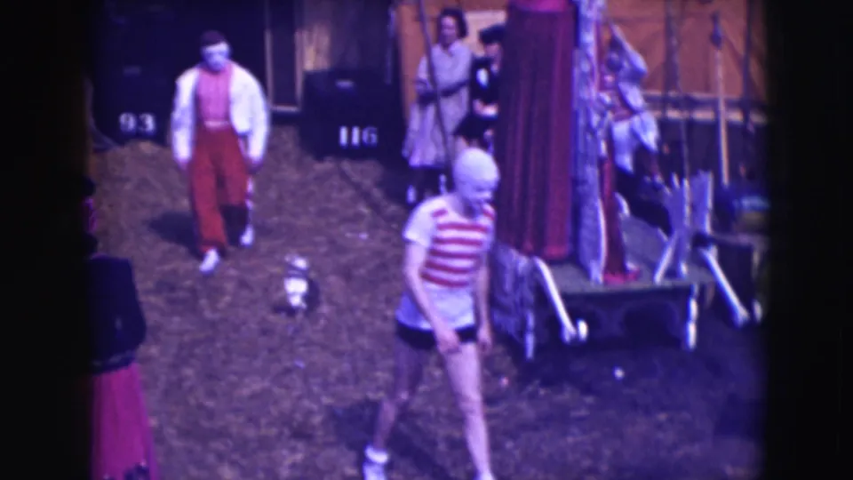 Ringling Brothers Sarasota backstage scene with a clown-like figure, another performer, circus wagons, and numbered trunks.