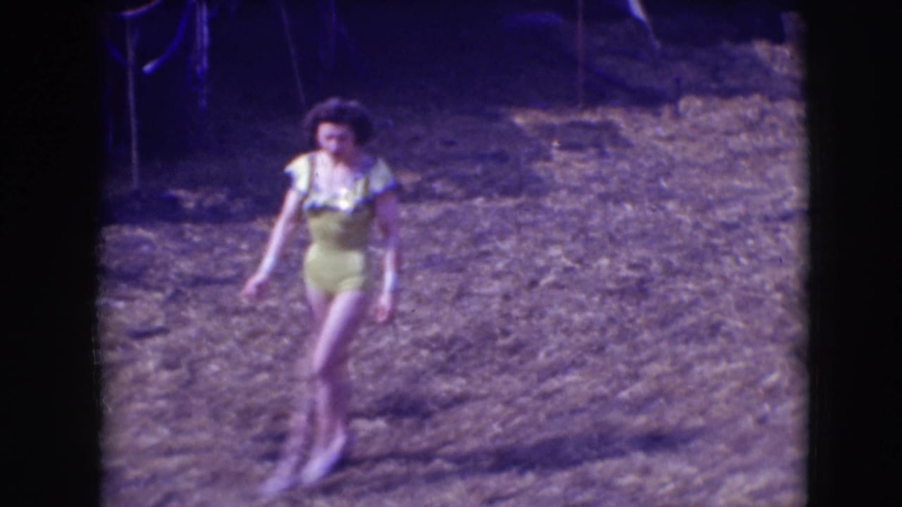 A 1948 Sarasota circus performer in a yellow ruffled costume moves through the outdoor dirt arena, seen in soft 8mm color.