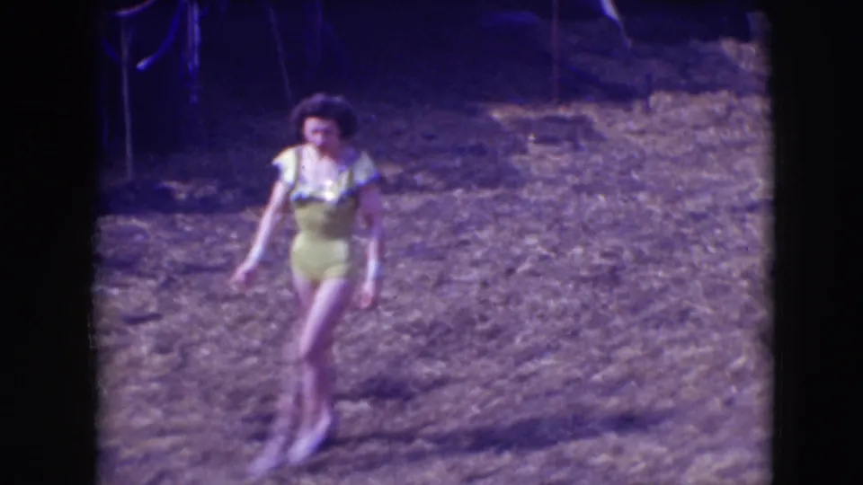 A 1948 Sarasota circus performer in a yellow ruffled costume moves through the outdoor dirt arena, seen in soft 8mm color.