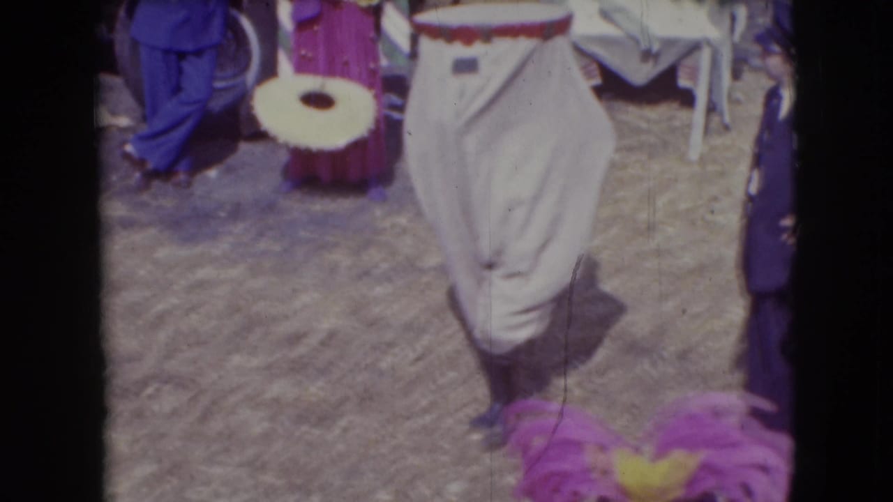 A white costumed figure crosses the Ringling Brothers Sarasota circus lot, with a drum-like object and other performers partly visible nearby.