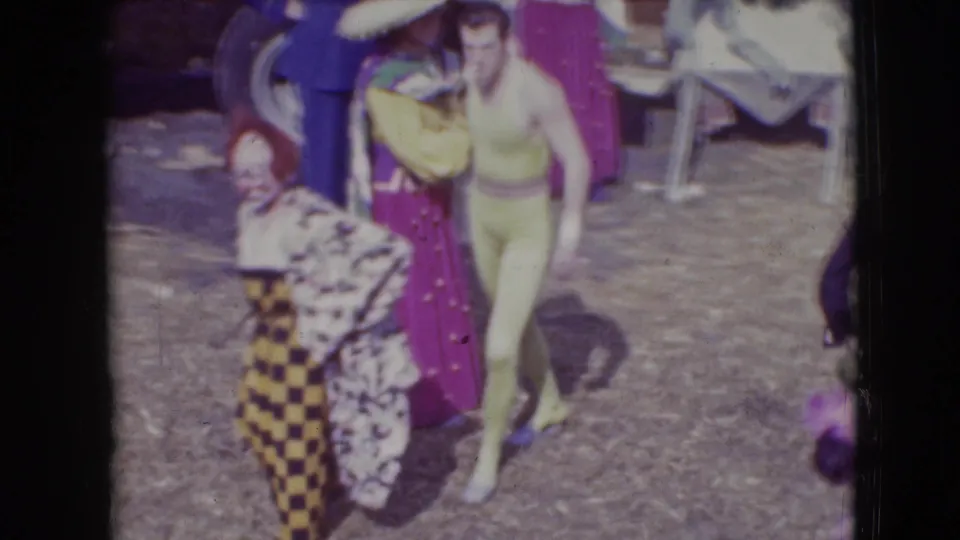 At the 1948 Sarasota circus lot, a checkered clown costume appears beside a performer in a yellow leotard and other colorful costumes.
