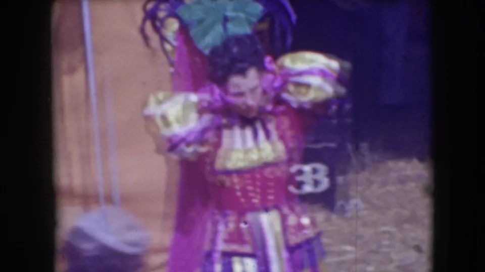 Backstage Ringling Brothers circus frame showing a male performer in red and gold costume near canvas tenting and numbered markers.