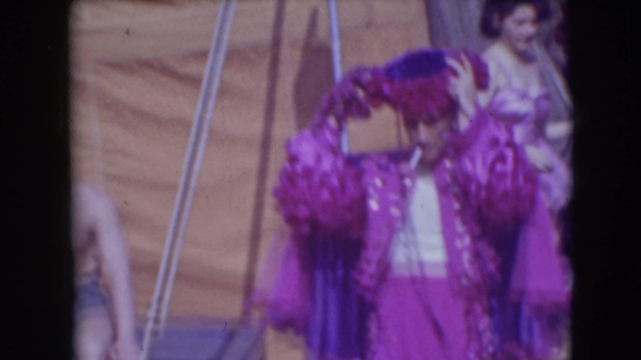Purple-costumed circus performer adjusting a feathered hat near backstage seating.