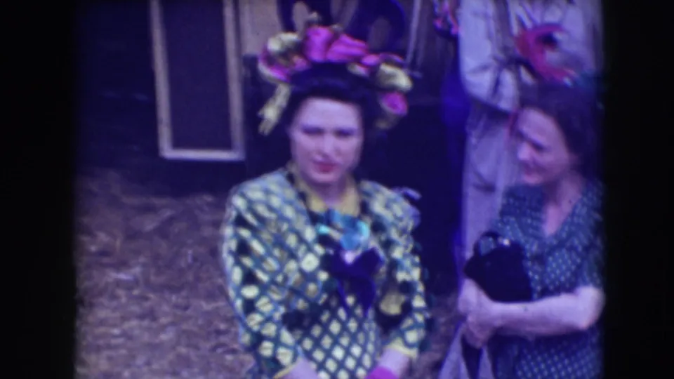 A woman in a patterned dress and ornate headpiece stands near another woman in a candid backstage circus scene from the supplied 1948 Sarasota clip.