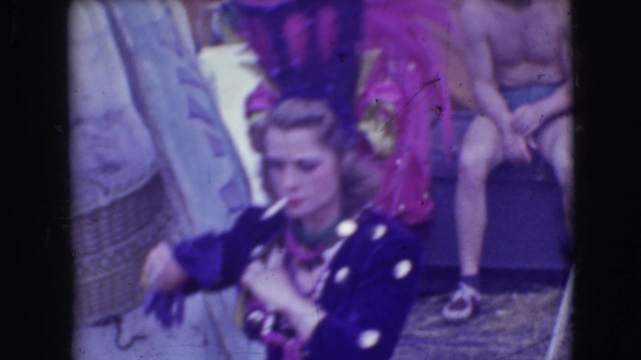 1948 Sarasota circus footage showing a costumed woman with a cigarette near seated spectators and performers in colorful attire.