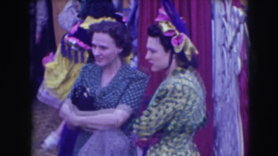 Two women smile beside a red curtain and a costumed performer during the 1948 Sarasota Ringling Brothers footage.