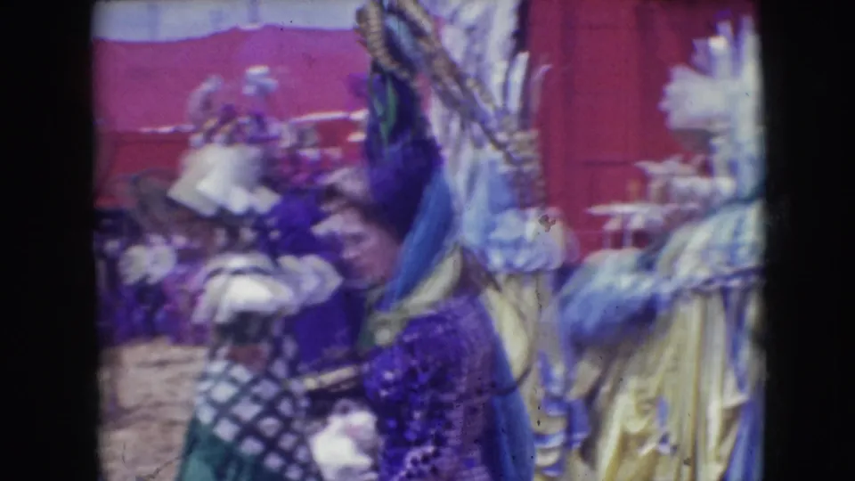 Close home-movie view of a Ringling Brothers performer in a purple feathered costume moving among other costumed women outdoors.