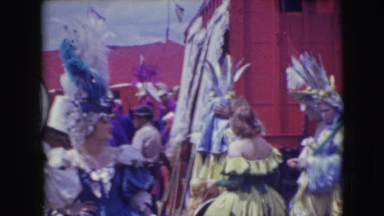 1948 Sarasota circus footage showing women in blue and yellow feathered costumes beside red wagons and white tents.